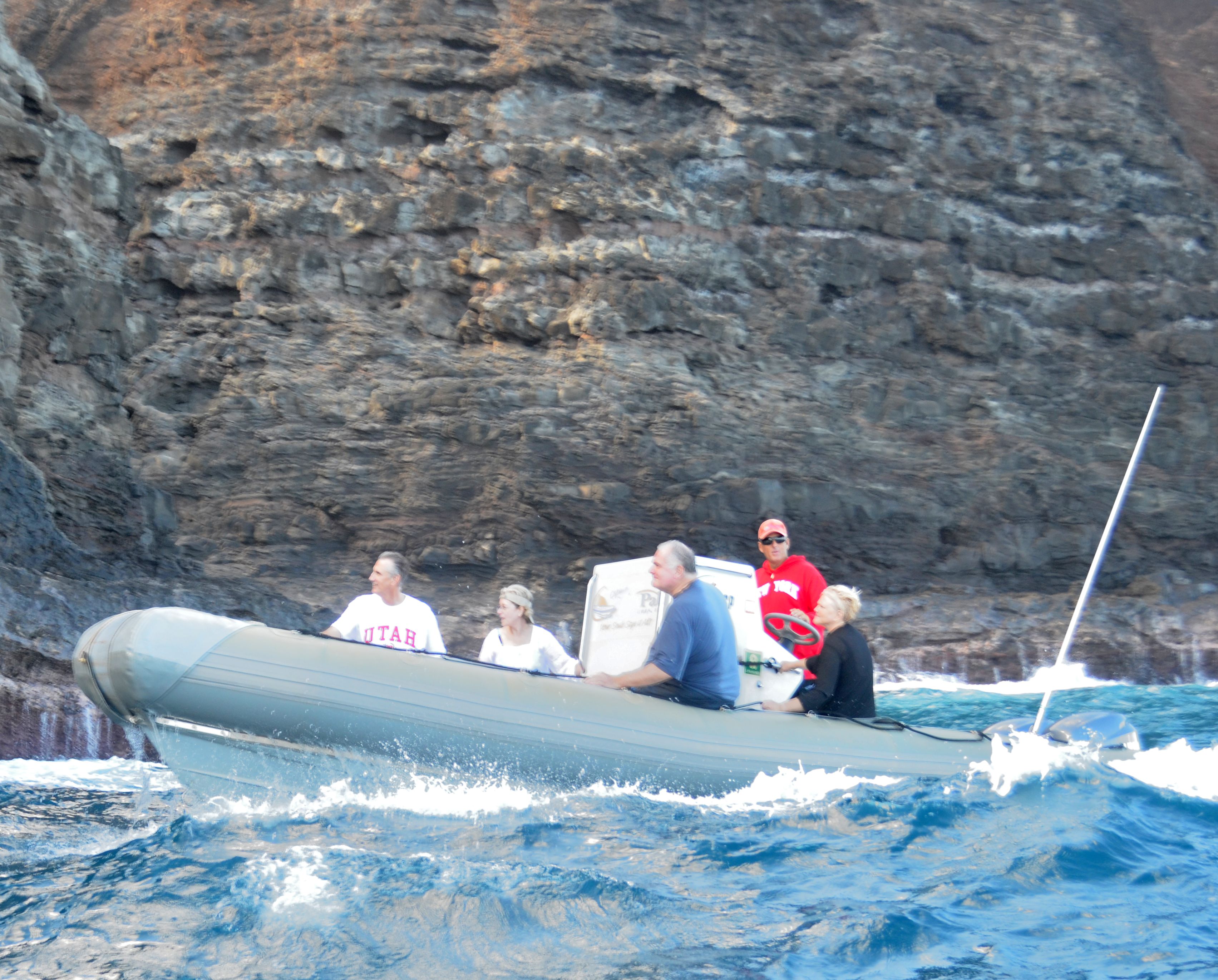 A Zodiac raft riding over a wave with guests holding on