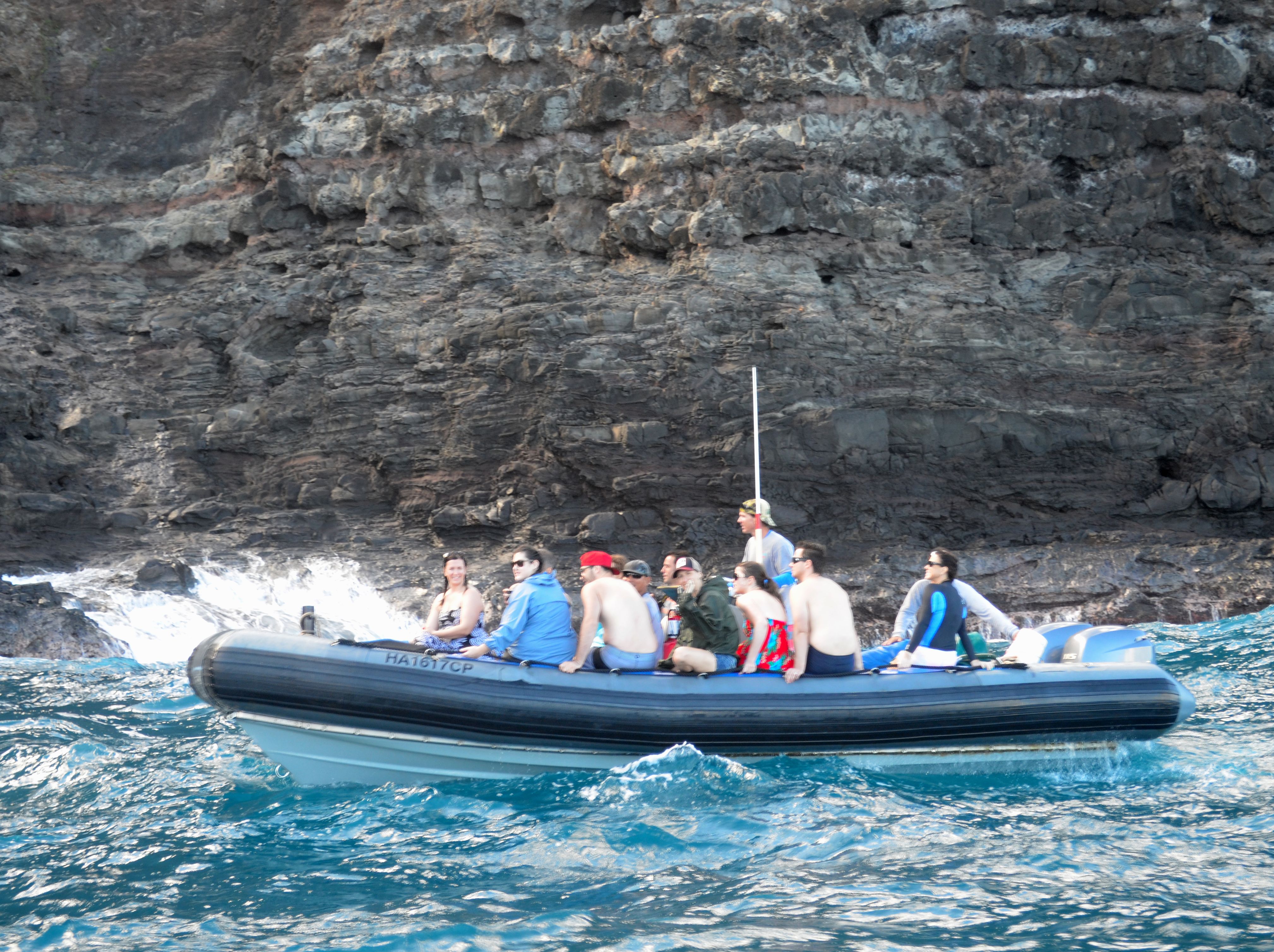 Guests seated on the inflatable side tubes of a Zodiac raft beside the Na Pali cliffs